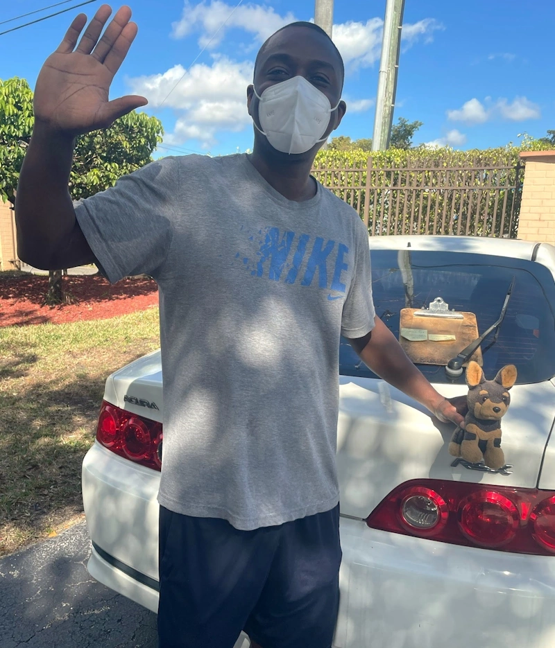 a person wearing a face mask waving in front of a car