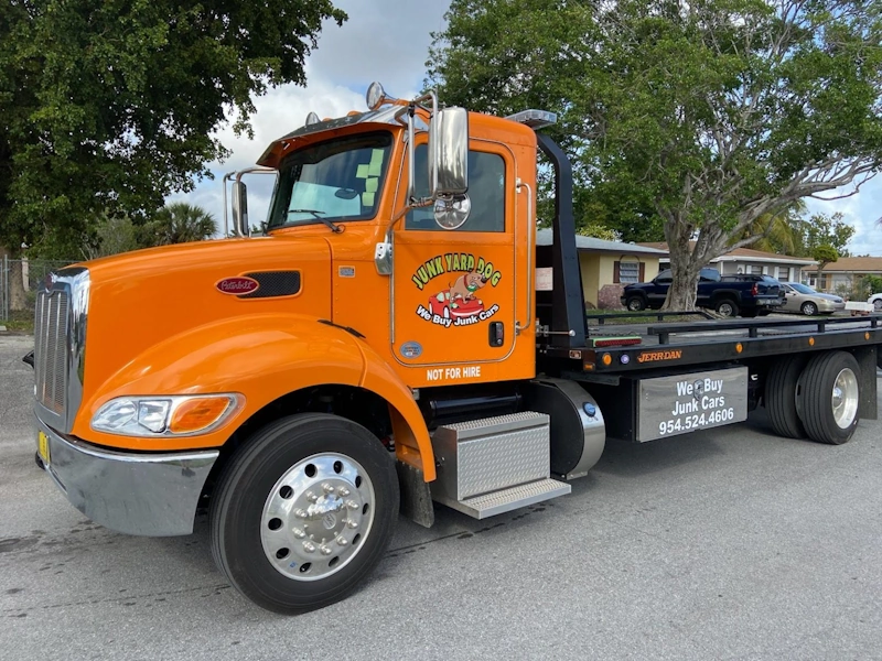 An orange flatbed tow truck parked on a street for a cash for junk cars in Oakland Park service.