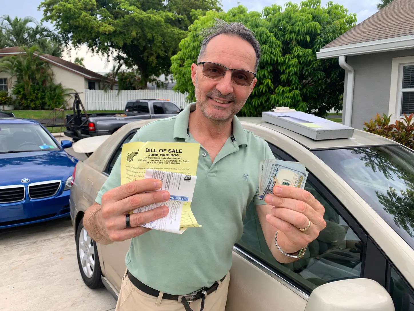 Seller holding cash and a Junkyard Dog bill of sale beside a car after pickup