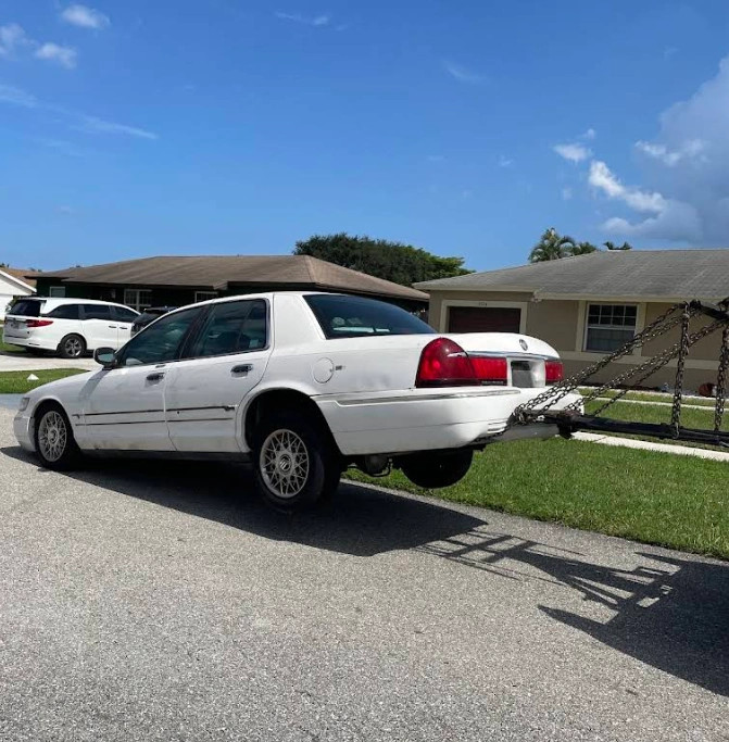 White sedan being towed away in a residential neighborhood for a Boca Raton sell my junk car service.